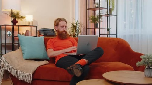Man with Red Beard Uses Laptop on Sofa