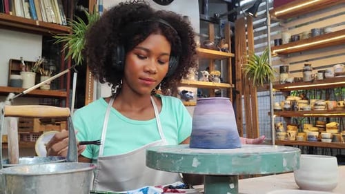 Females potter owners wearing apron sitting and painting a cup ceramics in pottery studio.