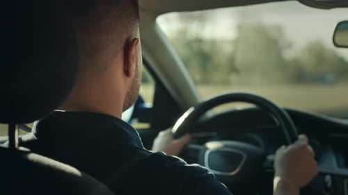 Man Driving Car Through Rural Farmlands on Sunny Day
