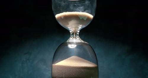 Reloj de arena con granos de arena sobre fondo oscuro. Filmado con una cámara a cámara superlenta de 1000 fps.