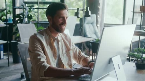 Smiling Man is Diligently Working on His Computer in a Contemporary Office