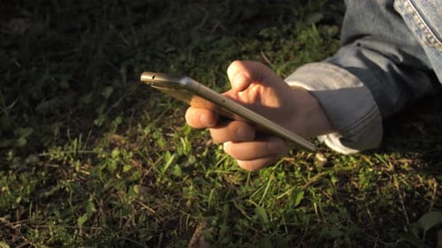 Close up of young woman's finger using he smartphone, grass and soil in the background