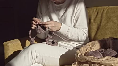 Woman knitting needles on the couch on a sunny day 4K