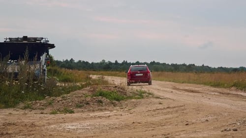 Red car driving on dirt road in countryside. View from behind as the vehicle goes away