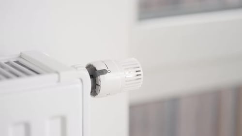 A man close the window and turns on the radiator of home heating to the maximum.