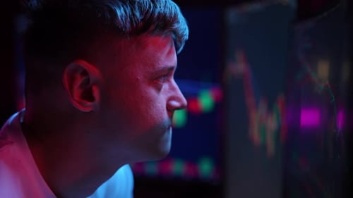 Stock Trader Intently Studying Stock Market Charts Illuminated By Colorful Glow of Multiple Monitors