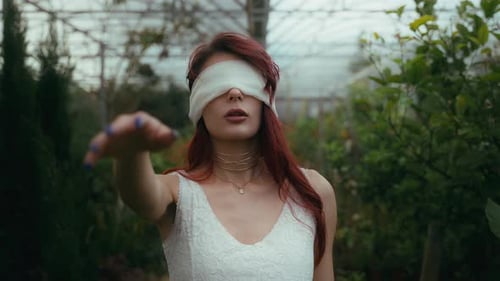 cinematic slow mo footage of young woman in a white dress and blindfolded walks with a stretched arm