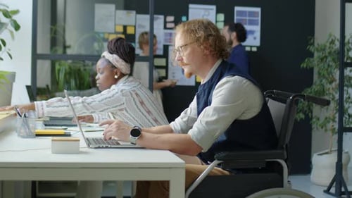 Man in Wheelchair Working on Laptop at Office Desk