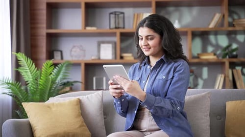 Young Woman Uses Tablet on Comfortable Sofa