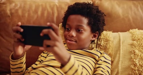 Boy Smiling, Using Smartphone on Couch Indoors