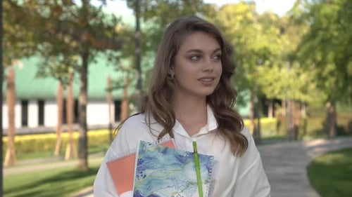 Young Woman Walking Outdoors with Notebook and Pen