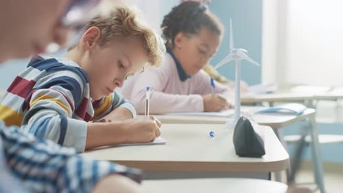 In Elementary School Classroom Brilliant Caucasian Boy Writes in Exercise Notebook, Taking Test and