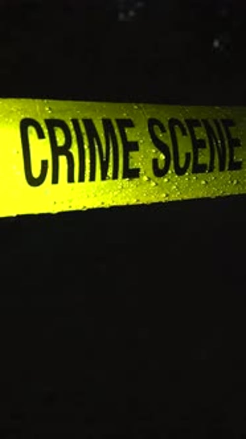 Police line Crime Scene tape in front of an evening outdoors area while raindrops fall on it slowly.