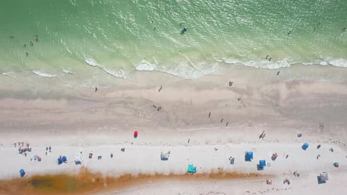 Aerial top-down view of turquoise shoreline with beachgoers and umbrellas