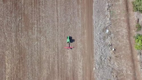 Green Tractor cultivating and seeding a dry field - Top down aerial footage