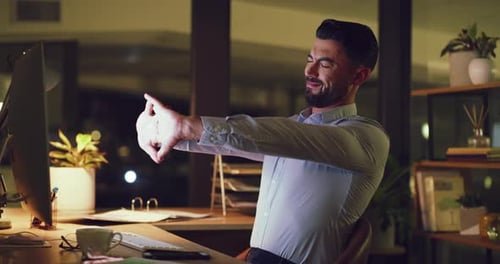 Man Stretching Hands at Computer in Dark Office