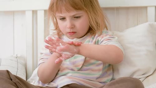 Baby Mädchen, das im weißen Schlafzimmer Feuchtigkeitscreme auf ihre Hand aufträgt, Kind trägt Lotion auf die Hände auf