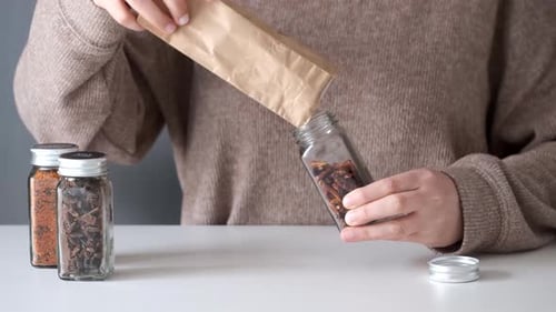 Woman Filling Spice Jar from Brown Paper Bag