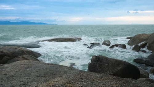 Waves Break on Dark Rocks Near Beach