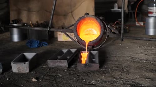 Slow motion bucket full of molten metal poured into moulds in a rustic foundry floor
