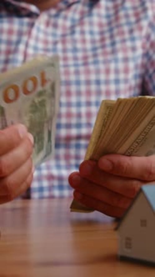 Man Counting Money Next to Model House on Table