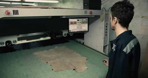 A Man in a Special Uniform Cuts the Right Pieces of Material with a Laser Machine at a Garment
