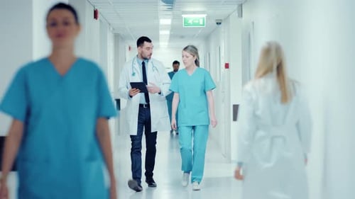 Surgeon and Female Doctor Walk Through Hospital Hallway, They Consult Digital Tablet Computer while