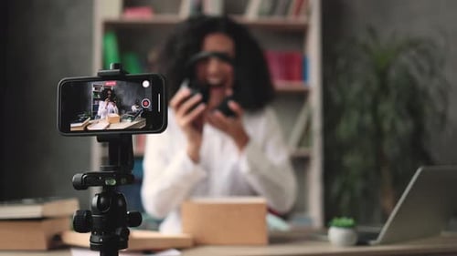 Focus on Smart Phone Screen Woman Recording Video on Phone Unpacking Box with New Headphones