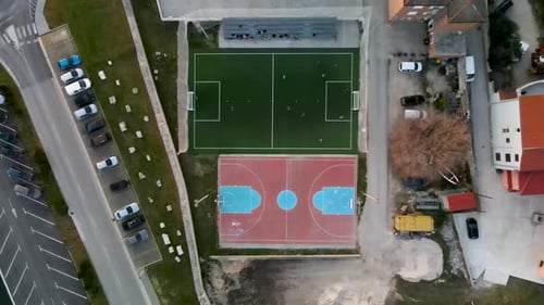 High Drone flight from bird's eye view over a small soccer field next to an basketball field where a