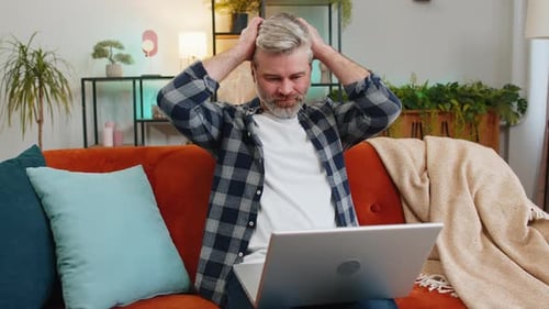 Man Using Laptop in Living Room, Looks Confused