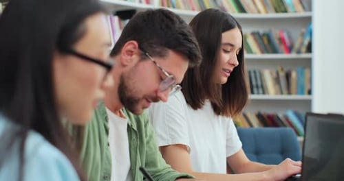 Des étudiants sympathiques assis à leur bureau en bibliothèque écrivent pour discuter d'un projet collaboratif préparant l'université