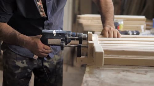 Adult Woodworker Drills Wood Planks in Workshop