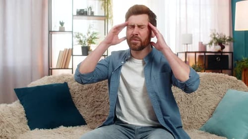 Man Rubs Temples, Suffering Headache on Couch
