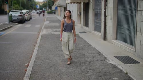 A Young Woman is Leisurely Walking Along an Urban Street Filled with Various Buildings