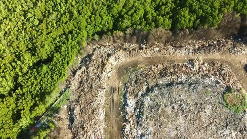 Aerial top view flying over road leading through huge landfill pile of dump and trash within mangrov