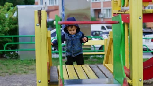 Sweet baby boy in a hood goes up by a ladder slowly.