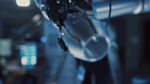 Close Up of a Futuristic Robotic Arm Moving a Metal Object and Placing It. Team of Engineers Observ