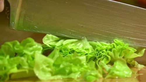 Knife cuts the lettuce in kitchen on wooden board. Close up.