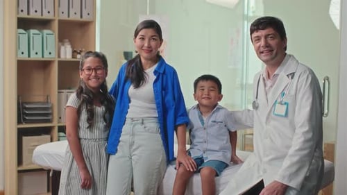 Doctor and Mother with Two Kids Looking at Camera during Visit at Clinic