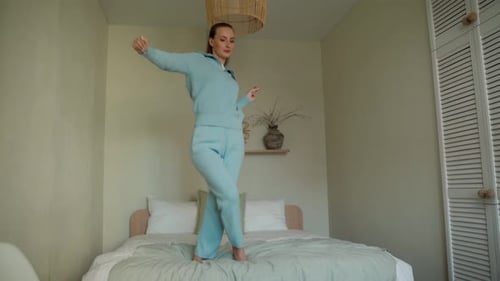 Happy Positive Young Woman Jumping Dancing on the Bed Experiencing Joy Alone in a Cozy Bedroom