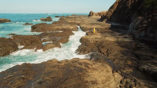 Aerial view of woman walking on rocky coastline beside tidal pools in Costa Rica