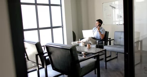 Talking on phone and using laptop, man working in modern office space