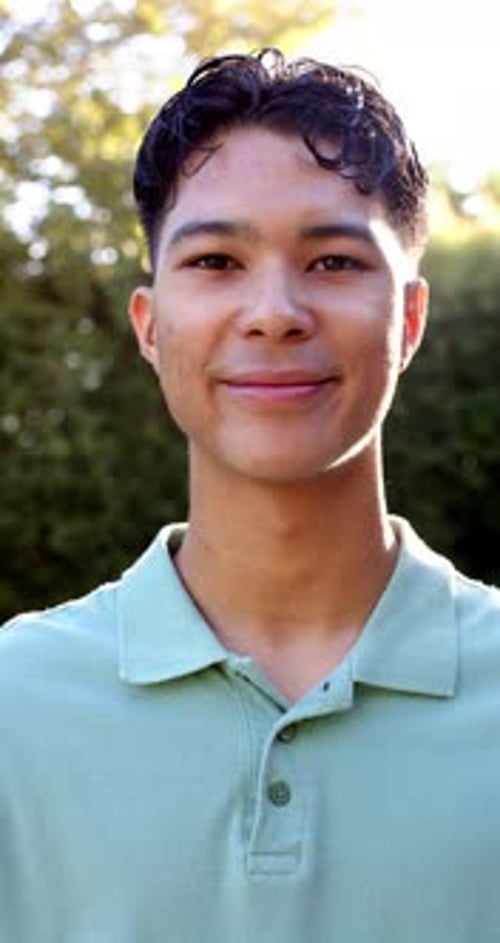 Vertical video: Smiling young man outdoors, wearing green shirt, enjoying sunny day