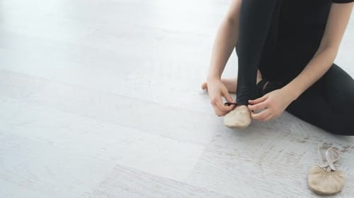 Young Adult Putting on Ballet Shoes on Floor