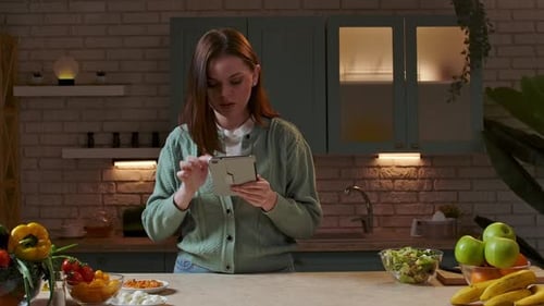 Woman Reads Recipe on Tablet in Kitchen at Night