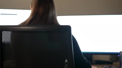 Woman Deep in Work on Modern PC Setup, Back View