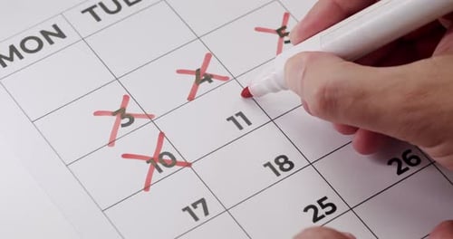 Person Crossing Out Dates On Calendar With Red Marker