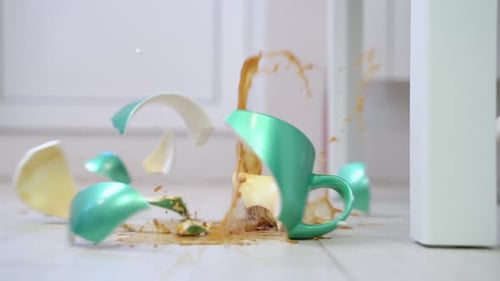 a cup of coffee falls to the floor from the table, breaks into many pieces.