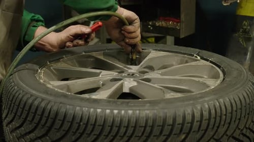 Close-up of Caucasian hands of a mechanic inflating a car wheel. Static