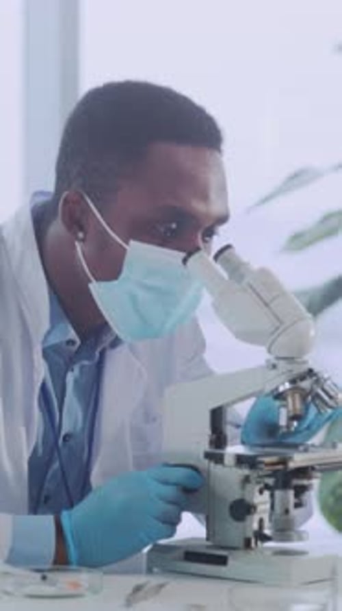Man in Lab Coat Looking Through Microscope